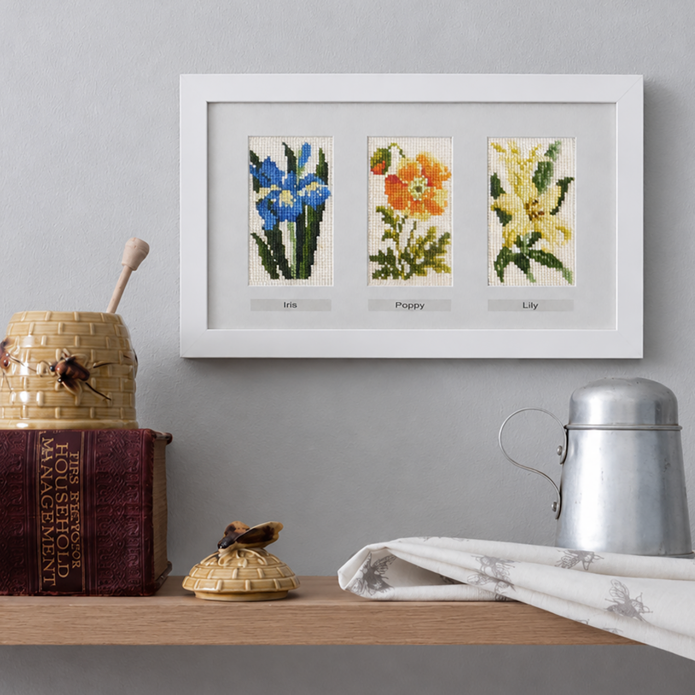Framed cross-stitch of flowers on a shelf with decorative items.