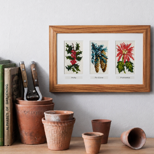 Framed winter foliage needlepoint of plants on a shelf with gardening tools and books